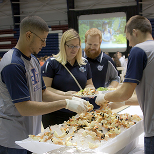 To the right, Johan Mejia and left, Devon Stubbings, student athletes at St. Thomas University, serve stone crabs to Melissa Hassell and her husband Johnny Hassell at the 6th Annual Stone Crab Dinner for Athletics.