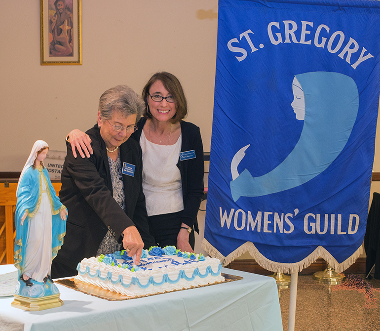 President Karen Wadowicz puts her arm around the shoulder of Irma Bengochea, who is cutting the 55th anniversary cake for the St. Gregory Women's Guild.