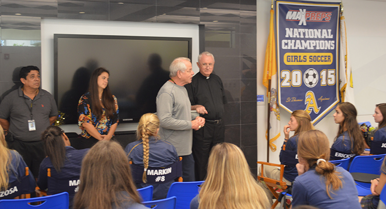 St. Thomas Aquinas athletic director George Smith, center, and Msgr. Vincent Kelly, right, congratulate the girls varsity soccer team on their back-to-back state championship. At left is soccer coach Carlos Giron.