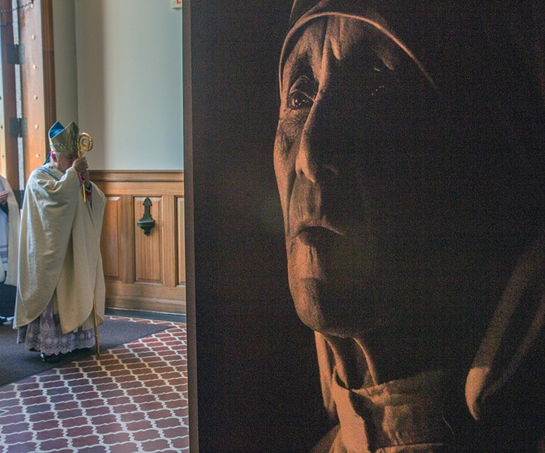 Archbishop Thomas Wenski pauses at the entrance to St. Mary's Cathedral before the Mass, as a photo of Mother Teresa is displayed in the foreground.