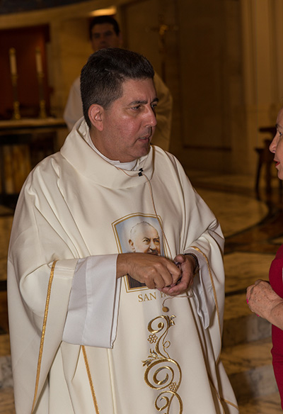 Wearing a vestment with the image of Padre Pio, Father Luis Garcia anoints the faithful with the oil of the sick.