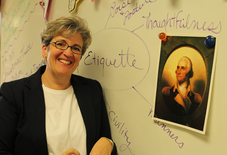 Surrounded by lessons in etiquette inspired by George Washington's character, Nativity School literature teacher Lynne Moore poses with an image of the first president. In Oct. 2016 Moore was invited to the George Washington Teacher Institute for a hands-on residency program that looked into the life and teachings of George Washington.