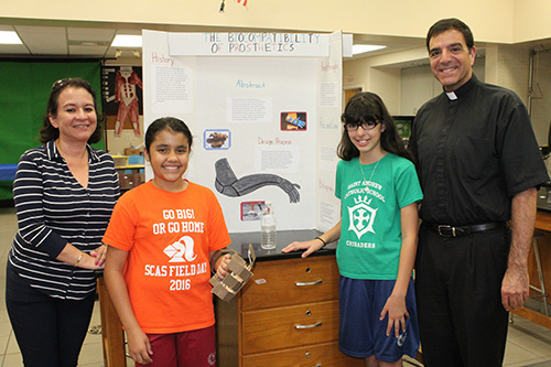 Getting an early look at prosthetics: Sixth graders Minnie Montañez, left, and Kiara Laurie researched and created a prosthetic arm for a class project. Standing with them is science teacher Renee Sarmiento and St. Andrew's pastor, Msgr. Michael Souckar.