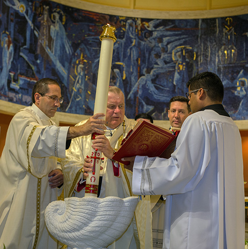 Archbishop Thomas Wenski dips the Paschal Candle in the baptismal font, blessing the water which will be used to baptize the catechumens who are joining the Church, during the celebration of the Easter Vigil at St. Mary Cathedral, March 31, 2018.