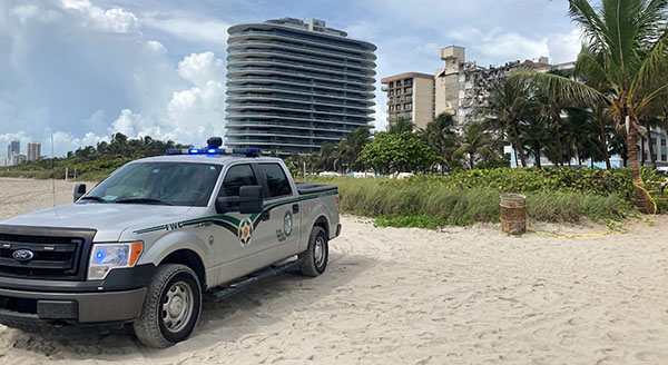 A Florida Fish and Wildlife Commission vehicle blocks access from the beach to the collapsed condo building in Surfside, visible in the background at right on the morning of June 25, 2021. A portion of the Champlain Towers South condominium, located at 88th Street and Collins Avenue, collapsed at 1:23 a.m. June 24, 2021, trapping dozens in the rubble.