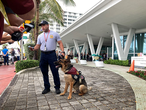 A fire rescue officer holds his search and rescue dog June 25, 2021 as he speaks to the media outside the Surfside Community Center, where families and friends gathered to await word on loved ones trapped in the rubble of the collapsed Champlain Towers South condominium in Surfside. A portion of the building, located at 88th Street and Collins Avenue, collapsed at 1:23 a.m. June 24, 2021, trapping dozens in the rubble.