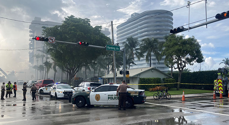 Police vehicles block off access as search and rescue operations continued June 25, 2021 on the site of the collapsed Champlain Towers South condominium in Surfside, visible in the background. A portion of the building, located at 88th Street and Collins Avenue, collapsed at 1:23 a.m. June 24, 2021, trapping dozens in the rubble.