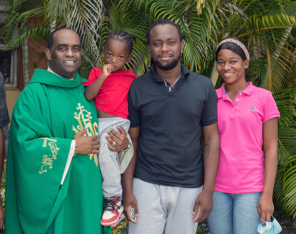 Father Reginald Jean Mary, Notre Dame d'Haiti's pastor, holds Kevin-Jay Metellus, 28 months old, while posing for a photo with his parents, Kervens Metellus and Marlene Belizaire, outside Notre Dame d'Haiti Church. All of them arrived from Texas around midnight Sept. 26, 2021.