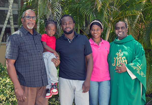 Notre Dame d'Haiti parishioner Baliston Elidor, far left, holds Kevin-Jay Metellus, 28 months old, while posing for a photo with the child's father, Kervens Metellus, and mother, Marlene Belizaire, and Father Reginald Jean Mary, Notre Dame d'Haiti's pastor. Elidor took the family into his home after they arrived from Texas, Sept. 26, 2021.