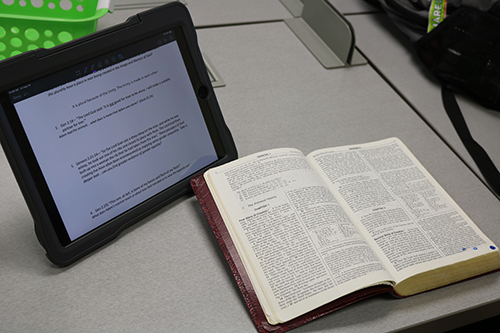 An Apple laptop and a Bible sit side-by-side on a desktop as one student studies in theology class at Cardinal Gibbons High School in Fort Lauderdale, Sept. 24, 2021.