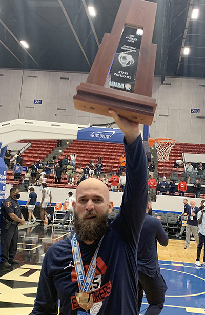 Head coach Andrew Moran triumphantly displays the state-championship trophy for Columbus fans after the Explorers' 45-44 victory over defending state champion Dr. Phillips, March 5, 2022, in the FHSAA Class 7A state boys basketball championship game at RP Funding Center in Lakeland.