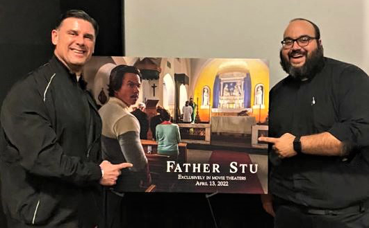 Father Rafael Capo, vice president of Mission and Ministry at St. Thomas University, and Father Matthew Gomez, director of the Office of Vocations at the Archdiocese of Miami, pose with the movie poster of "Father Stu" at the advance screening of the film on March 1, 2022 at the AMC Sunset Place theater in South Miami.