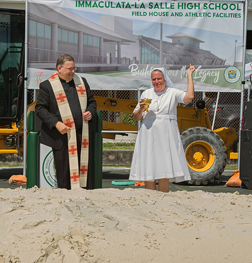 La Hna. salesiana Kim Keraitis, directora de la escuela secundaria Immaculata- La Salle, bendice el suelo mientras el P. Jesús Ferras, párroco de la iglesia vecina de St. Kieran, observa, durante la ceremonia de colocación de la primera piedra, para la construcción de una nueva pista de atletismo e instalaciones deportivas, el 1 de junio de 2022.