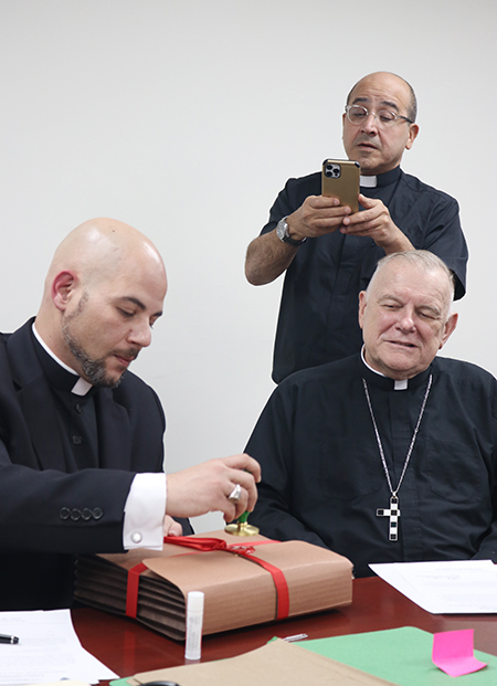 As Archbishop Thomas Wenski looks on, Father Luis
Rivero, episcopal delegate, seals the original results of
the investigation into a presumed miracle that took place
in Miami attributed to Venezuela's Blessed José Gregorio
Hernández, June 17, 2022, at the archdiocesan Pastoral
Center in Miami.
