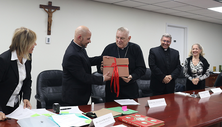 Archbishop Thomas Wenski hands over the original sealed documents of the investigation of the alleged miracle attributed to Blessed José Gregorio Hernández to Father Luis Rivero, episcopal delegate, so that he can deposit them in the archive of the Archdiocese of Miami, June 17, 2022. Looking on are Msgr. Dariusz Zielonka, archdiocesan chancellor for canonical affairs, and Dr. Beatriz González del Castillo, a physician who served as an expert in the investigation.