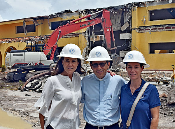 Leaders of the building campaign for St. Agnes pause as machinery demolishes the old building July 26, 2022. From left are Anabel Stevens, business manager; Father Juan Carlos Paguaga, the pastor; and Marcela Zamora Erana, head of the building fund.