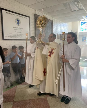 Father Luis Flores carries a monstrance with the Blessed Sacrament through the hallways of Sts. Peter and Paul School in Miami, Aug. 22, 2022.