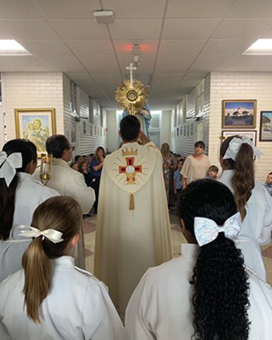 Father Enzo Rosario Prendes carries the monstrance with the Blessed Sacrament through the hallways of Sts. Peter and Paul School in Miami, Aug. 22, 2022.