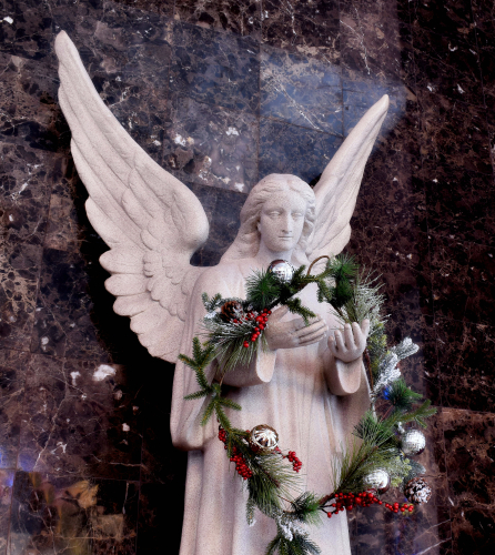 Someone whimsically placed a Christmas wreath in the hands of an angel statue.