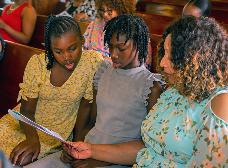 Orielle Small, 10, Khloe Small, 12, and their grandmother, Kum Roy, read the Black Unity Prayer from the church bulletin at the conclusion of the Unity Mass sponsored by the archdiocese's Black Catholic Ministry, June 25, 2023.