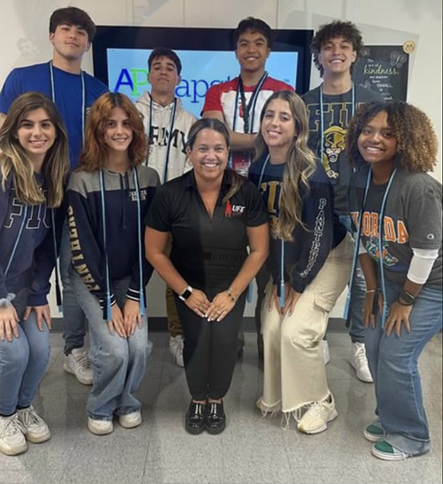 Jamie Argüello, standing in the bottom row at the far right, poses with fellow Msgr. Edward Pace High School students wearing the AP Capstone cords they earned.