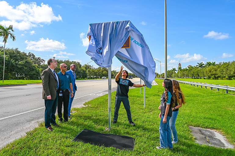 As his siblings, Sophia and Susanna, and school officials watch, Christopher Inguanzo unveils the new street sign that marks the entrance to Archbishop Edward McCarthy High School along Flamingo Road in Southwest Ranches, Aug. 14, 2023. Watching, from left: Catholic schools Superintendent Jim Rigg; McCarthy High Principal Kevin Molina; and school President Richard Jean.