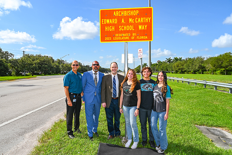 Posing under the new street sign that marks the entrance to Archbishop Edward McCarthy High School along Flamingo Road in Southwest Ranches, from left: McCarthy High Principal Kevin Molina and school President Richard Jean;Catholic schools Superintendent Jim Rigg; and the McCarthy High siblings who spearheaded the effort: Susanna, Christopher, and Sophia Inguanzo. The dedication and unveiling took place Aug. 14, 2023.