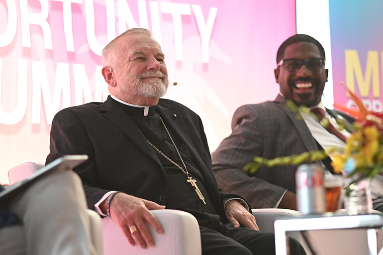 Archbishop Thomas Wenski prepares to take part in the Miami Opportunity Summit: Immigrant Contributions and Bipartisan Solutions, a daylong series of panel discussions mingling local politicians, journalists, social workers and business leaders with representatives of Catholic charitable agencies, held Aug. 22, 2023, in Miami. Next to him is Rodrick Miller, president and CEO of the Miami-Dade Beacon Council.