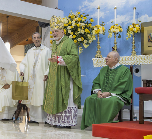El P. José Luis Paniagua, administrador y párroco de la iglesia St. Benedict en Hialeah de 1989 a 2018, recibe un regalo del Arzobispo Thomas Wenski, durante la Misa del 50 aniversario de la parroquia, el 23 de septiembre de 2023.
