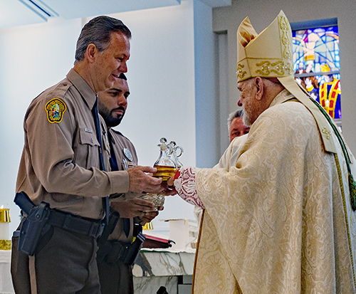 Archbishop Thomas Wenski receives the offertory gifts of bread and wine from Miami-Dade police officers David Greenwell, executive vice-president of the South Florida PBA, and Detective Ricaurte Lugo during the Blue Mass, Sept. 29, 2023, at Our Lady of Guadalupe Church in Doral.