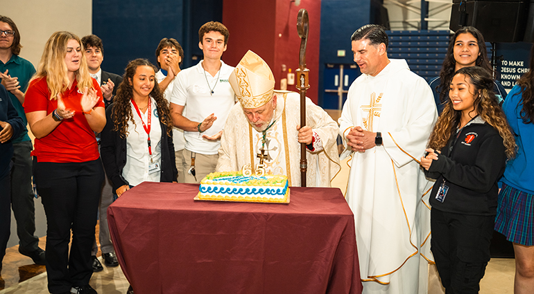 Surrounded by students representing the different archdiocesan high schools, Archbishop Thomas Wenski blows out the candles on the Archdiocese of Miami's 65th anniversary cake, as Father Rafael Capo, vice-president of Mission and Ministry at St. Thomas University looks on. The birthday bash was part of "Rise Up for a Revival!" on the university's campus, Oct. 5, 2023.
