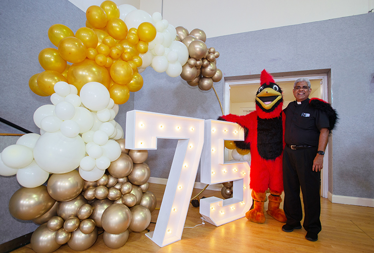 Father George Packuvettithara, pastor, poses with the school mascot, a cardinal, after the Mass closing St. Rose of Lima Parish's 75th anniversary celebration, Oct. 15, 2023. Under the costume: Nico Barreiros, 14, a graduate of St. Rose of Lima School who now attends St. Thomas Aquinas High School in Fort Lauderdale.