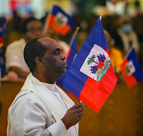 Father Reginald Jean-Mary, pastor of Notre Dame d'Haiti Mission in Miami, carries the Haitian flag in procession as participants prepare to walk around the church at the conclusion of the third of seven nights of Jericho, Oct. 15-21, 2023.