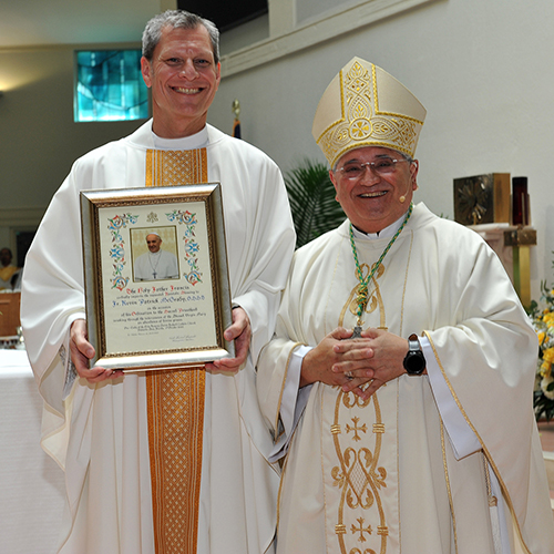 Auxiliary Bishop Enrique Delgado poses with Trinitarian Father Kevin McGrady, who is holding a papal blessing, after ordaining him a priest Oct. 7, 2023, at the parish where he will first serve, Our Lady of the Holy Rosary-St. Richard in Cutler Bay.