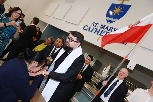 Newly ordained Father Piotr Sawicki imparts a first blessing to a well-wisher after the Mass where Archbishop Thomas Wenski ordained him and three others, May 11, 2024 at St. Mary Cathedral. Behind Father Sawicki is Jan Wolniak, who carries a Polish flag as a guard of honor. Wolniak was part of a group of about 30 Poles who attended the ceremony.