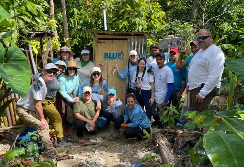 A group from St. Brendan High stands with a new latrine they helped build while on a BLUE Missions trip in March 2024 to La Pieza, Dominican Republic.