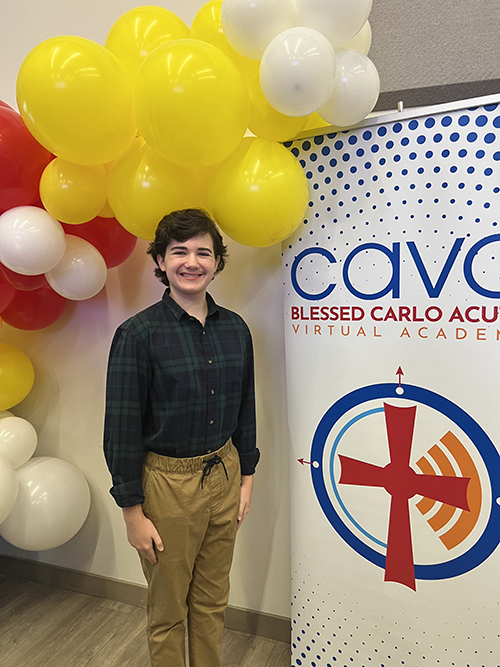 Parker Dillon, a rising 9th grader at Blessed Carlo Acutis Virtual Academy (CAVA), poses with the school banner at the CAVA Inaugural Mass and Blessing Ceremony May 29, 2024, at St. Brendan High School in Miami.