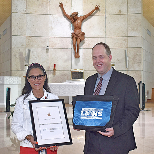 Teresita Wardlow, principal of St. Mark School in Southwest Ranches, shows the designation as an Apple Distinguished School conferred on Sept. 11, 2024. With her is Jim Rigg, superintendent of schools for the archdiocese, with a laptop bag given him as a gift for attending the event.