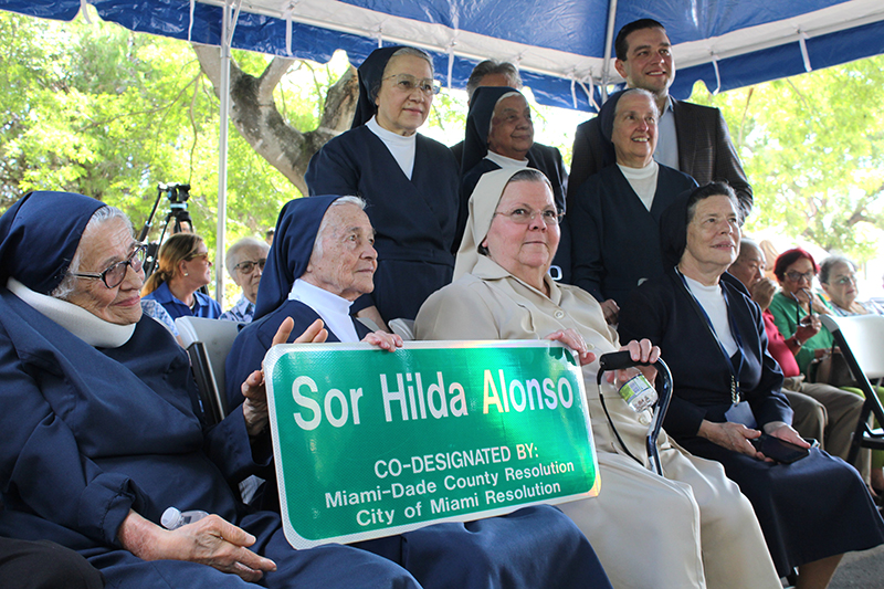 Las Hijas de la Caridad de San Vicente de Paúl de Miami sostienen el letrero de Sor Hilda Alonso en el acto de homenaje a la madre fundadora de la orden. Desde la izquierda, abajo, Sor Clemencia Fernández, Sor Rafaela González, Sor Olga Gómez, y Sor Reynalda Ramírez. De pie, Sor Milagros Olivencia, Sor Juanita Flores, el Comisionado Miguel Angel Gabela, el Miembro de la Junta del Consejo Comunitario del Condado de Miami-Dade, Dariel Fernandez, y Sor Eva Perez-Puelles.