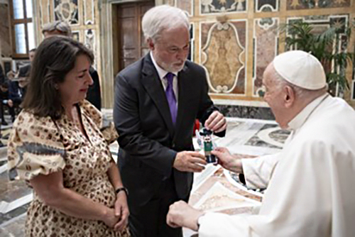 Coral Gables Commissioner Kirk Menendez gifts Pope Francis with a cut-out of Louis the Musketeer, the mascot of St. Theresa School, during a conference held at the Vatican in August 2024. Menendez and his wife Maria Teresa (also in the photo) are parishioners of Church of the Little Flower in Coral Gables.