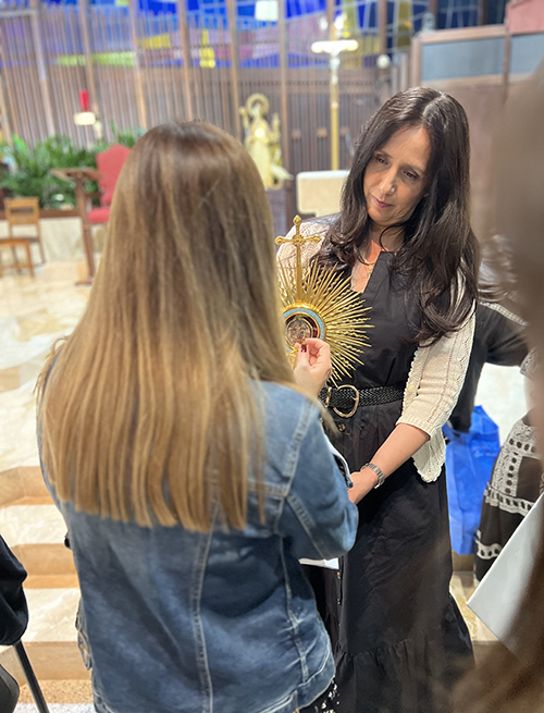 Marcela Martinez De Torres, a volunteer, holds the reliquary containing the first-class relics of seven saints, including the veil of the Blessed Mother, while a member of the faithful holds a religious object to the reliquary during the Sacred Relics Exposition and Veneration at St. Hugh Parish Nov. 3, 2024.