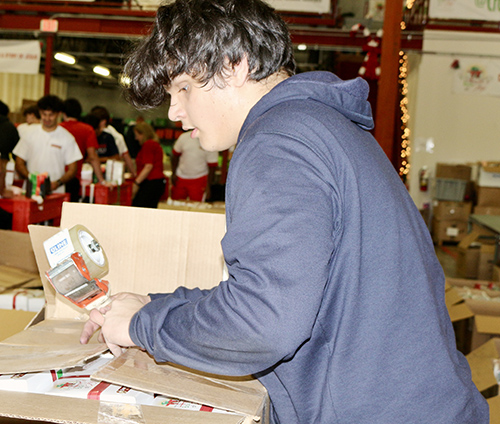 Giorgio Picasso, a 9th grader at Christopher Columbus High, tapes shut a cardboard box full of “Boxes of Joy” for underprivileged children at Box of Joy National Screening Center in Doral Dec. 12, 2024. Students from the Stand for the Silent anti-bullying club screened box contents and prepared them for shipping.