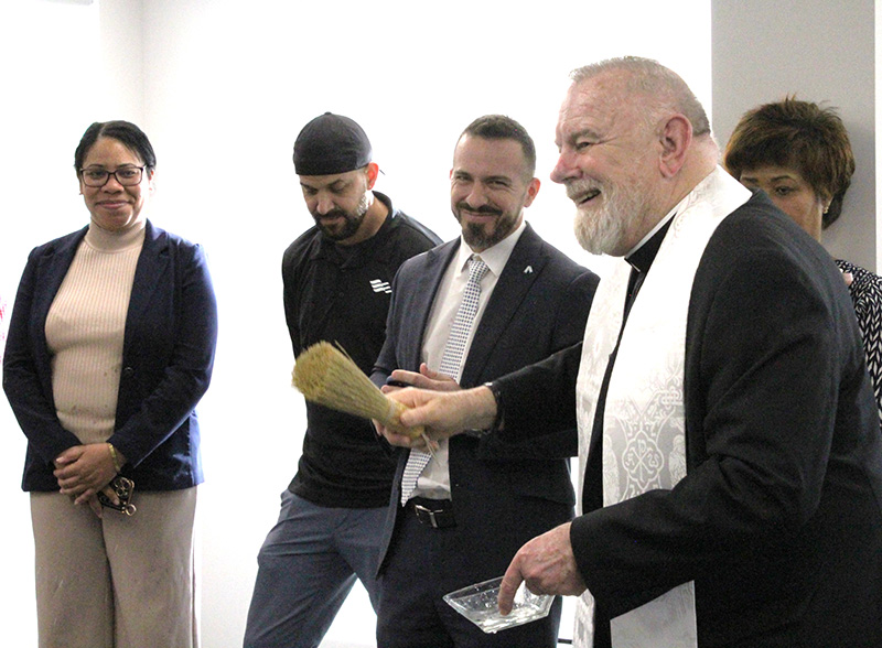 Archbishop Thomas Wenski smiles as he blesses the staff of  of Catholic Legal Services with holy water at the blessing ceremony of its new Miami location on Jan. 15, 2025.