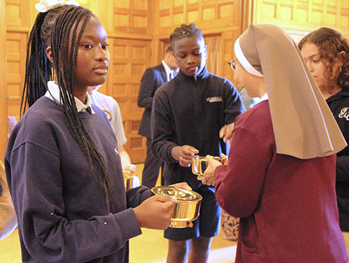 Before the start of the All Schools Mass at St. Mary Cathedral in Miami, Jan. 29, 2025, Malika Auguste (left) of Holy Family School in North Miami practices carrying the bread for the offertory. Adewale Dada of St. Jerome School in Fort Lauderdale also receives the bread from Sister Mary Martha Cuenca.