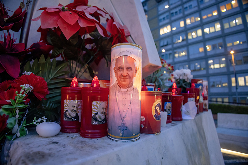 Votive candles and flowers are seen at the base of a statue of St. John Paul II outside Rome's Gemelli hospital Feb. 19, 2025, where Pope Francis is being treated for double pneumonia.