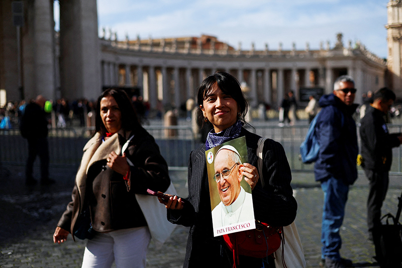 A woman smiles as she holds an image of Pope Francis in St. Peter's Square at the Vatican Feb. 26, 2025, as he continues his treatment for double pneumonia at Rome's Gemelli Hospital. The 88-year-old pontiff had a "restful night" and was sitting upright in an armchair, the Vatican said early Feb. 26.