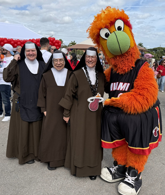 Sister Mary Patrice, Sister Mary Elizabeth, and Principal Sister Rosalie Nagy, Carmelites who serve St. Theresa School in Coral Gables, take a photo with Miami Heat mascot Burnie at the school's Pig-Nic event on Jan. 26, 2025.