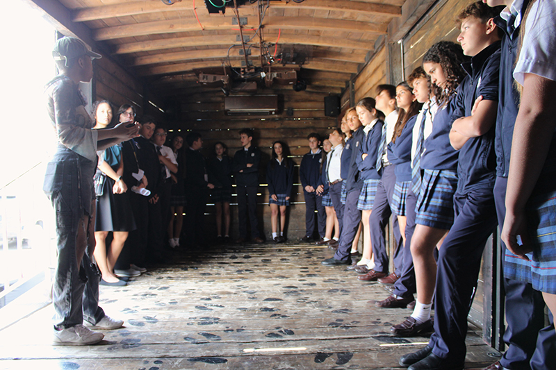 St. Louis Covenant School seventh graders listen to Raven McClendon before they experience the Hate Ends Now Cattle Car Exhibit film shown from within the cattle car during the Holocaust Remembrance Day event held March 3, 2025.