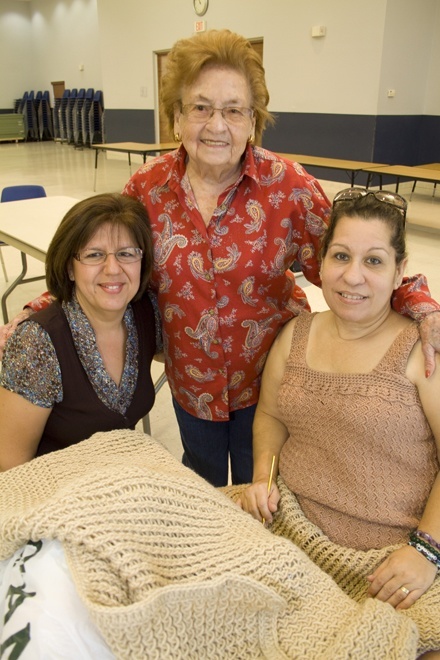 Maria Benitez, de 91 aos, parada en el centro, revisa un lapghan que teje Gina Moya, sentada a la derecha. Con ellas est otro miembro del grupo Puntadas de Amor, Marlene Lopez.