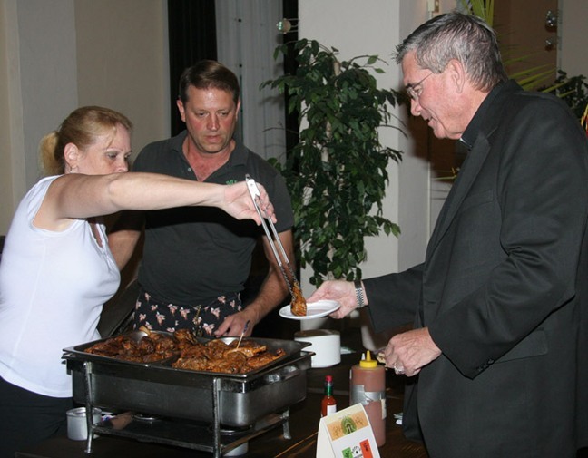 Father Arthur Dennison, Little Flower's pastor, takes a "Taste of the Gables" during the fundraiser for St. Theresa School's athletic program.